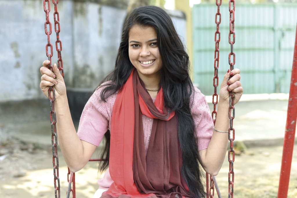 18 year-old girl smiles while sitting on a red swing.