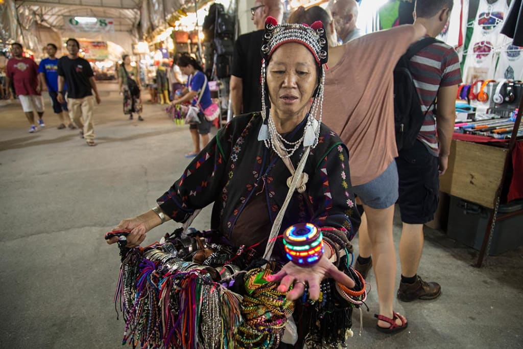 A woman dressed in traditional Thai garb sells trinkets at a Thai night market.