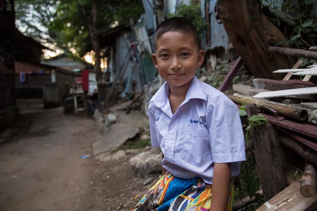 A Thai boy sits in front of a home in a village slum.