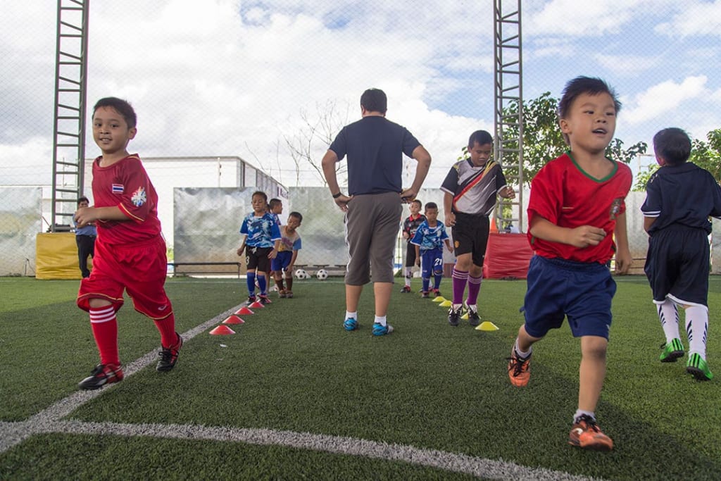 Boys run soccer drills on a soccer field as their coach looks on.