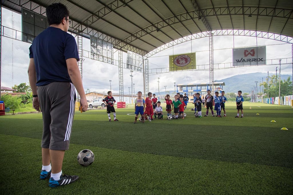 A soccer coach stands at the end of a covered soccer ball, preparing to kick the ball to his team.