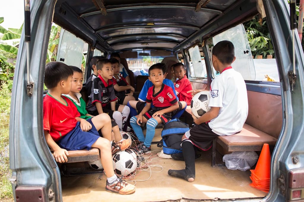 Young boys sit in the back of a van dressed in soccer uniforms, ready to play.