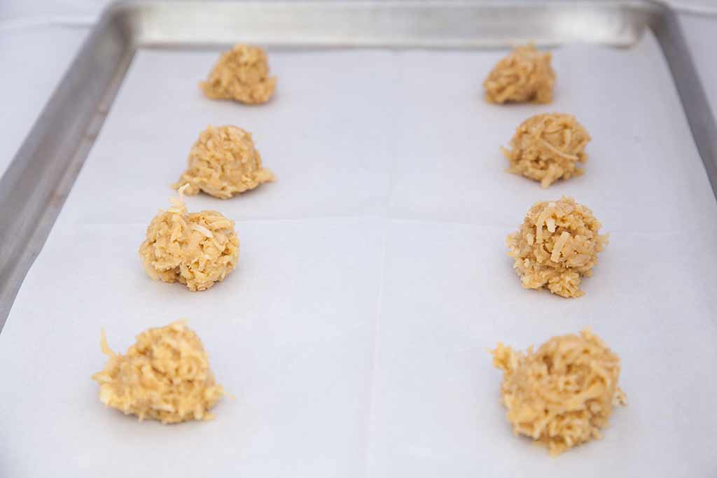 A cookie sheet lined with parchment paper, with balls of cookie dough on it.
