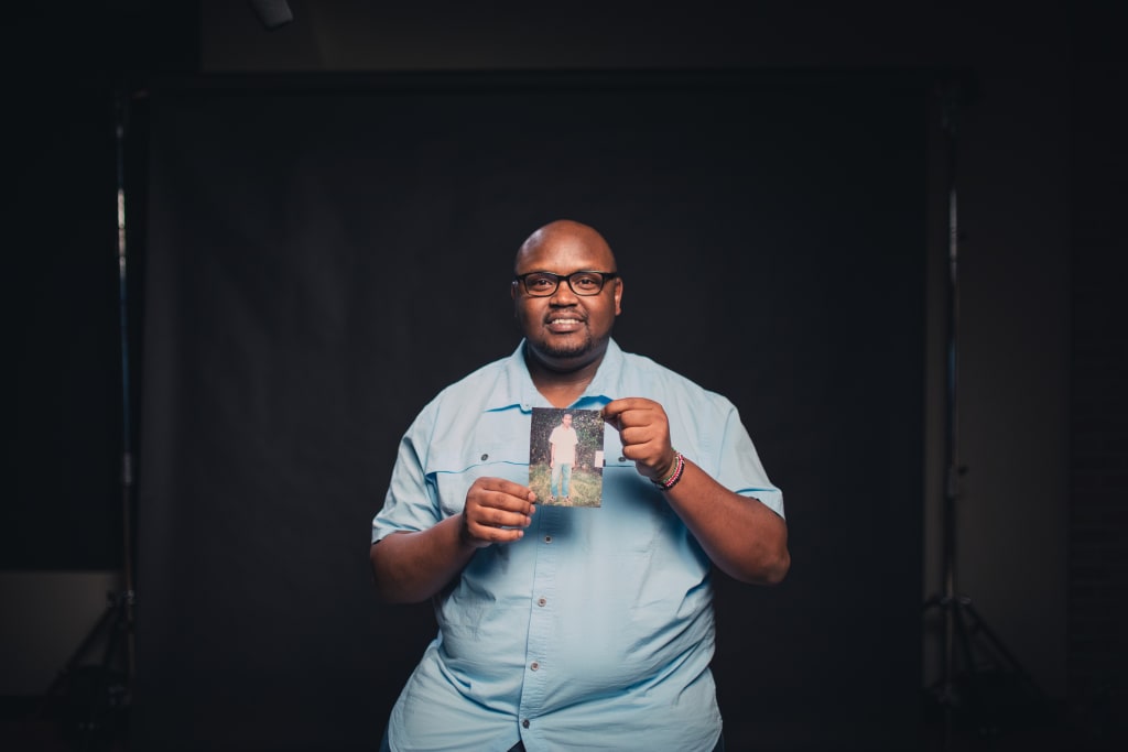Owen, a Compassion alumnus from Kenya, is wearing a light blue shirt. He is holding up a picture of himself as a child.