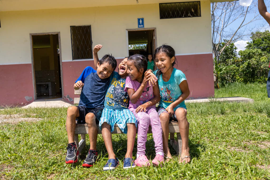 Fausto , Jairo, Scarleth, and Valeria are sitting on a bench outside. They are celebrating clean water at their Compassion centre.