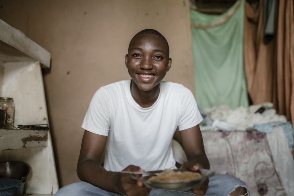 A teen boy in a white shirt holds a bowl of food and smiles with joy.