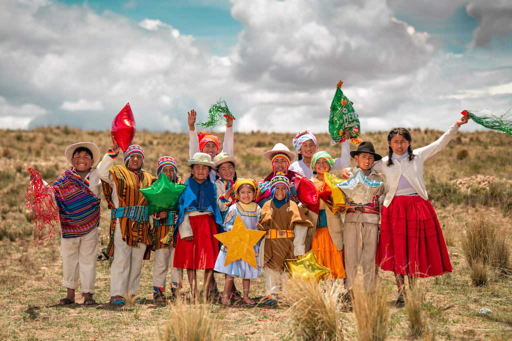 Kids from Bolivia wearing different colours and holding up balloons. They are celebrating the arrival of Jesus who is ushering in the upside-down Kingdom of God.