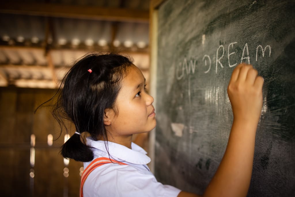 A girl writes "I can dream" on a chalkboard. She is wearing a school uniform.