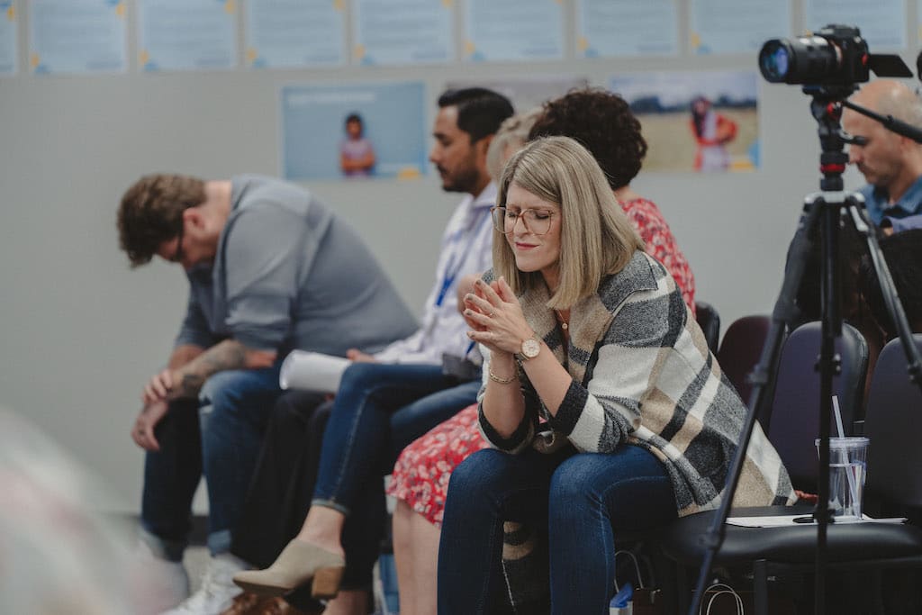 Allison Alley sits amongst Compassion Canada staff with her eyes closed and hands folded in prayer.
