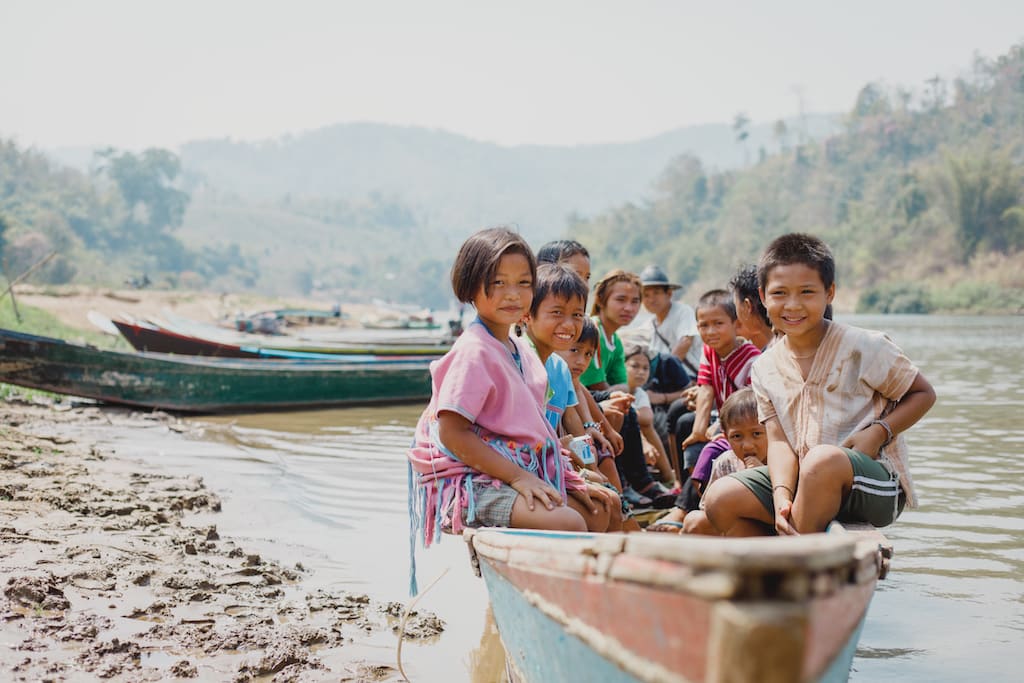 A group of children in Thailand, in a boat on the shore of a river.