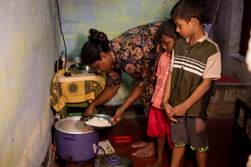 A woman bends over a pot of rice while two young boys stand watching her.
