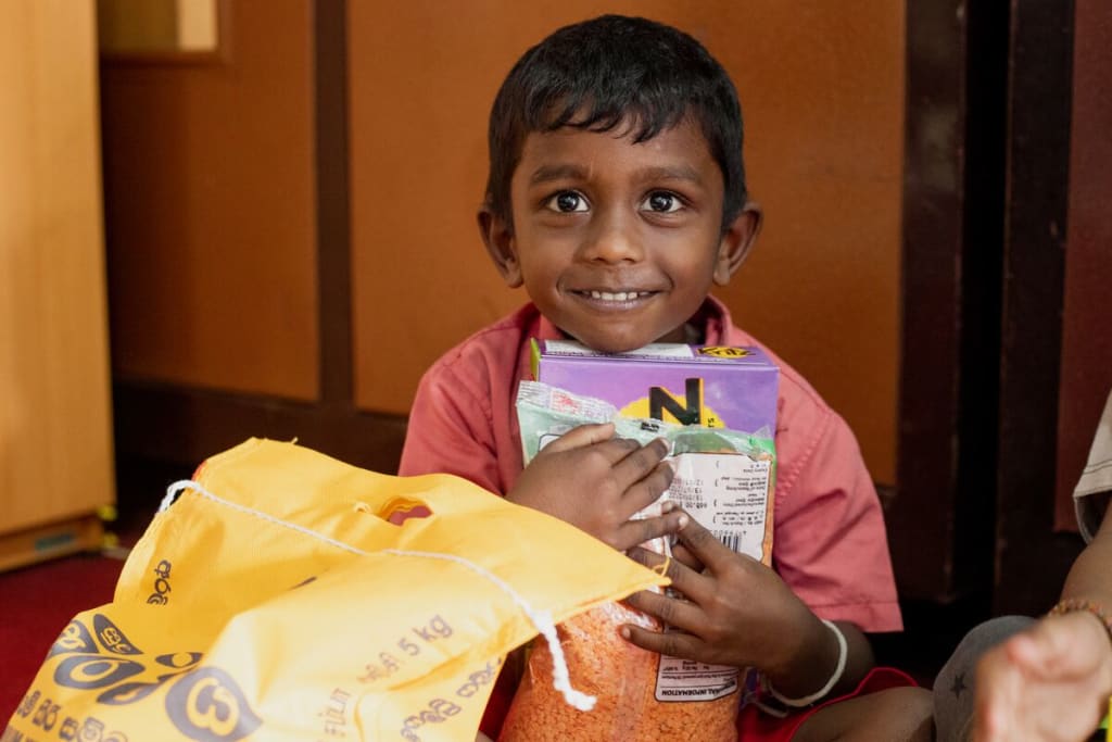 A little boy in a red shirt holds a packet of food and smiles