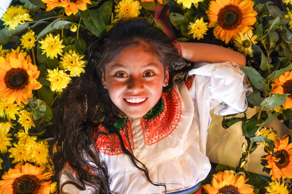 Girl smiles lying in a field of flowers.