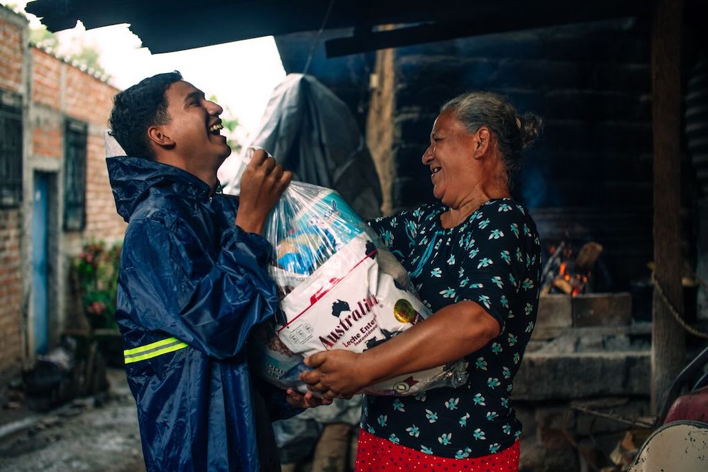 A boy in El Salvador hands a bag of groceries to an elderly neighbour.
