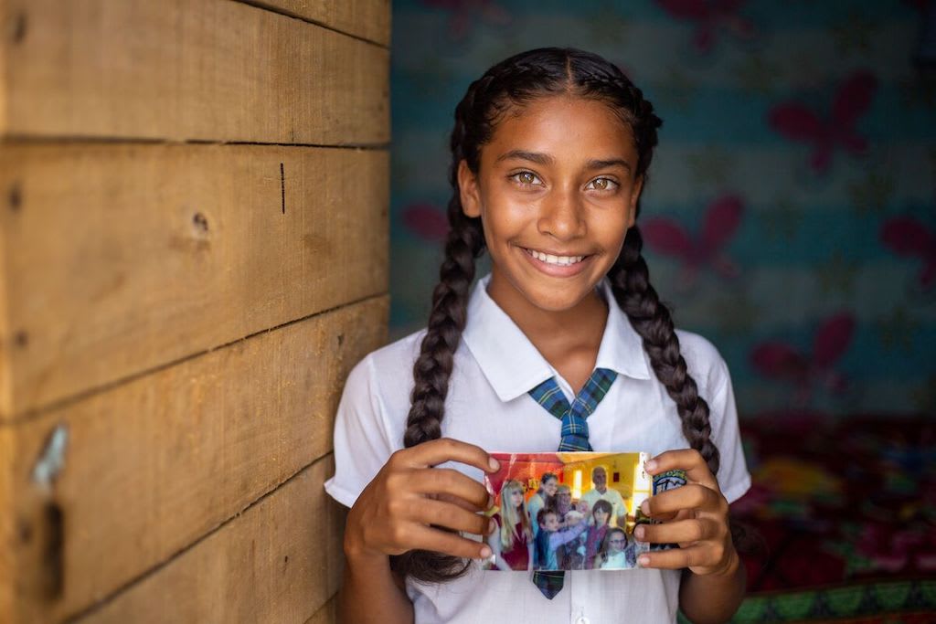 A girl in Colombia holds up a photo of her sponsors