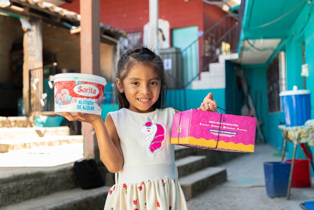 A girl holds up a tub of ice cream and a cake box