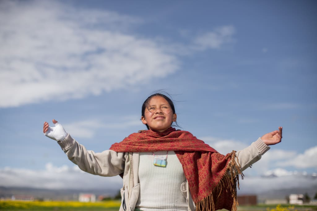 Girl from Bolivia wears a red scarf and opens her hands to the sky in prayer
