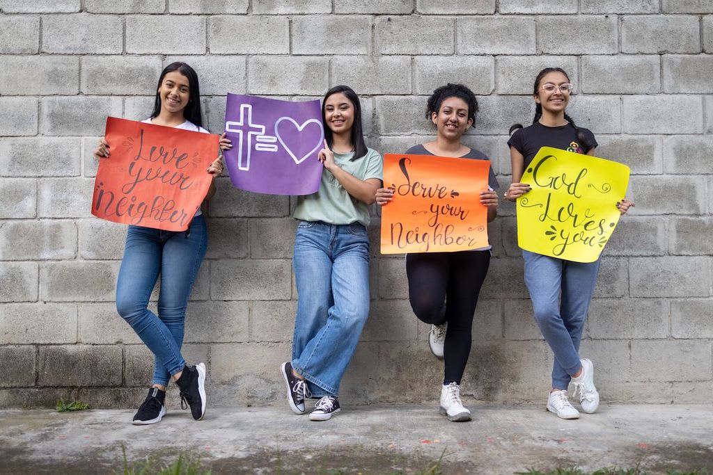 Teen girls hold signs that say "love your neighbour"