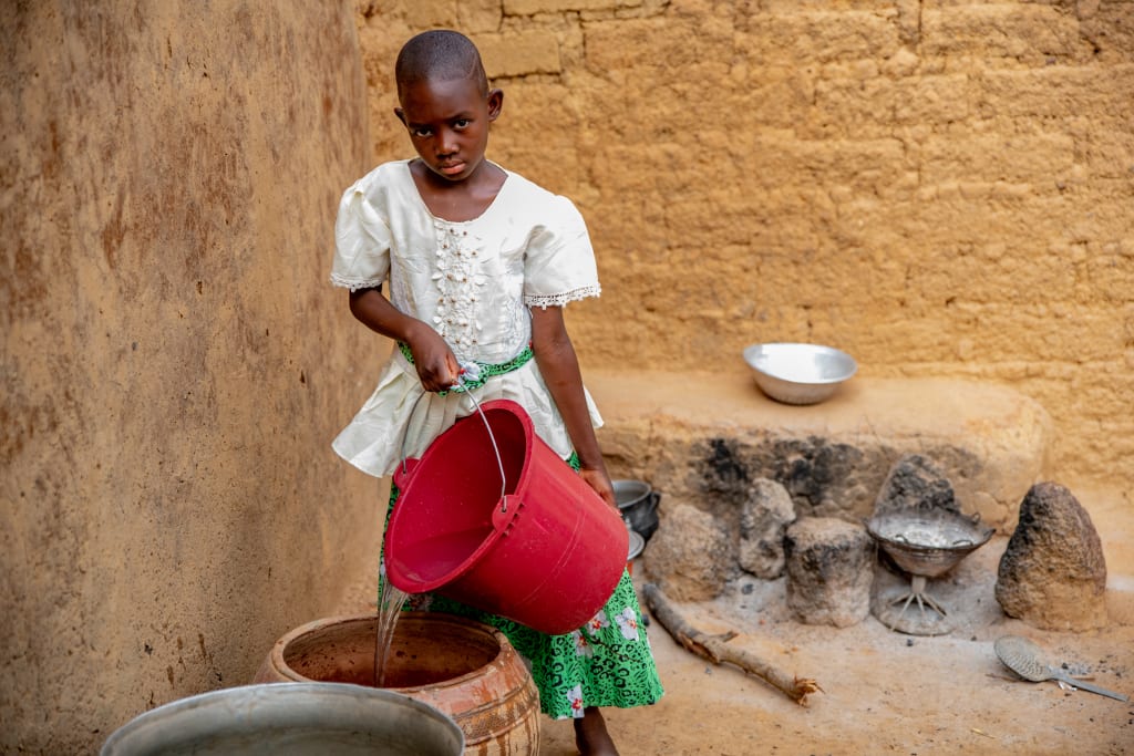 A young girl in a white top pour water out of a red bucket.