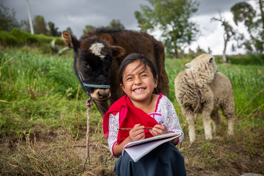 Girl sits in front of a furry cow holding a notebook. She is smiling big.