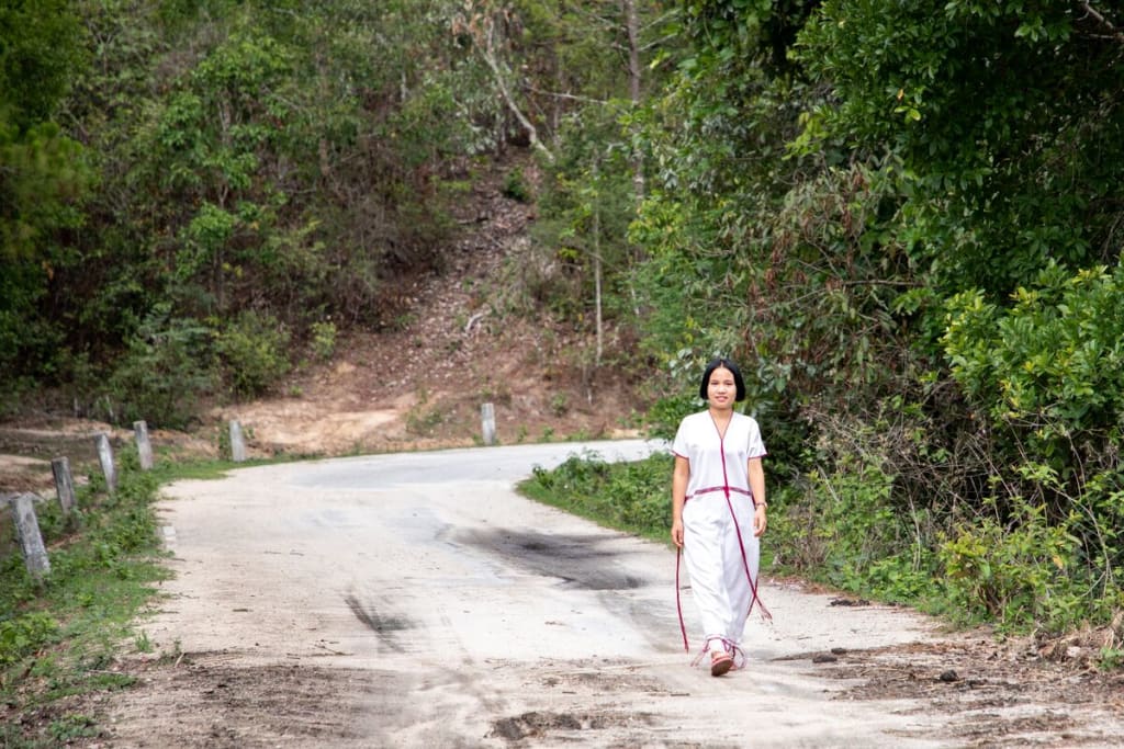 A teenage girl wearing all white walks on a dirt road