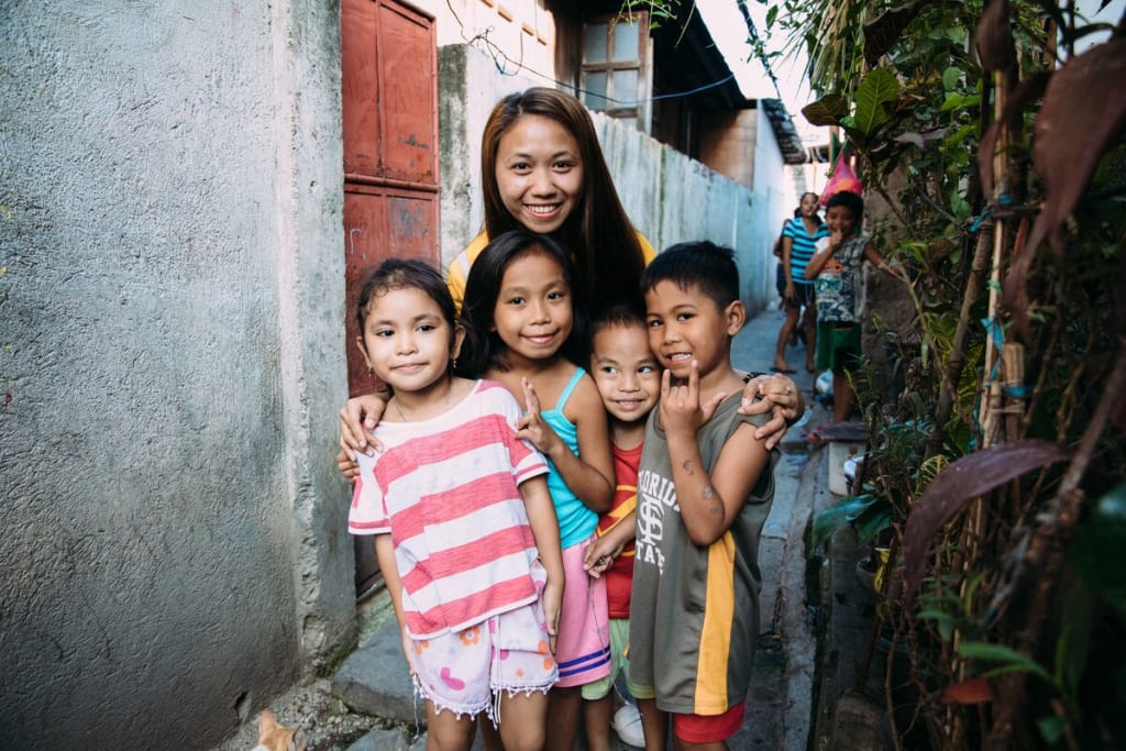 A woman stands with four children in an alley. They are all smiling.