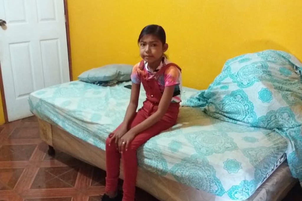Francis is earring a t-shirt and pink overalls, sitting on a bed in her new room, which is painted bright yellow. This clean and safe space will allow her to receive her life-saving medical care, dialysis, in the comfort of her own home.