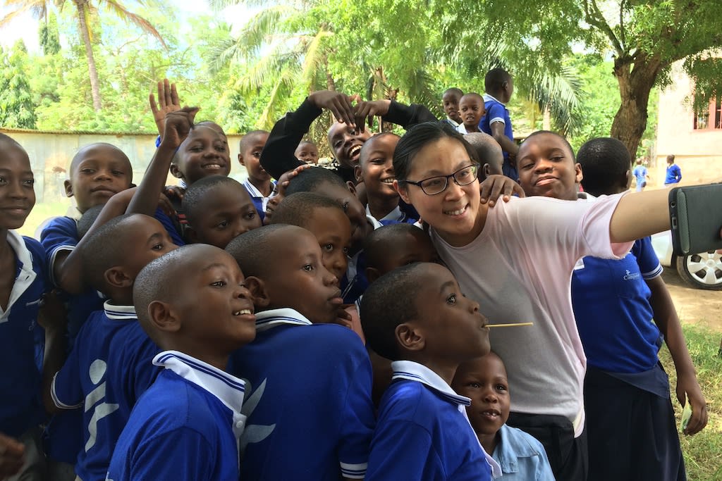 Andrea stands amongst a group of children in blue school uniforms, taking a selfie with the group.