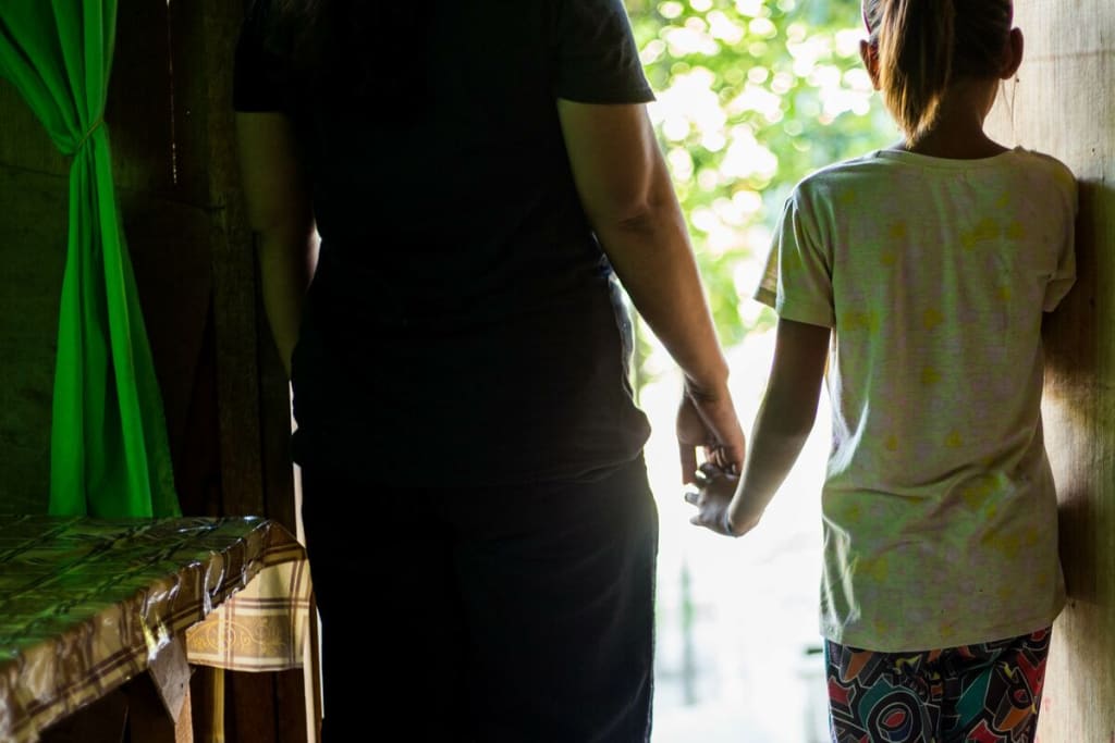 A mother and daughter stand in their home; their identities are concealed.