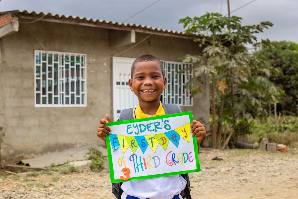 Eyder stands in front of his home holding a card that says "Eyder's first day of third grade".