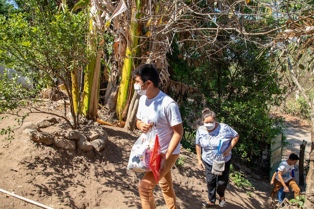 A group of volunteers walks up a steep hill with groceries. They are wearing masks.