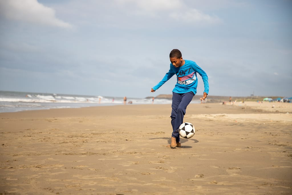 A boy kicks a soccer ball on a beach.