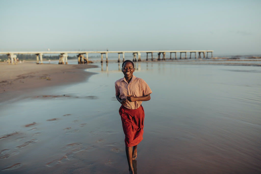 A young woman runs along the shore of a beach.