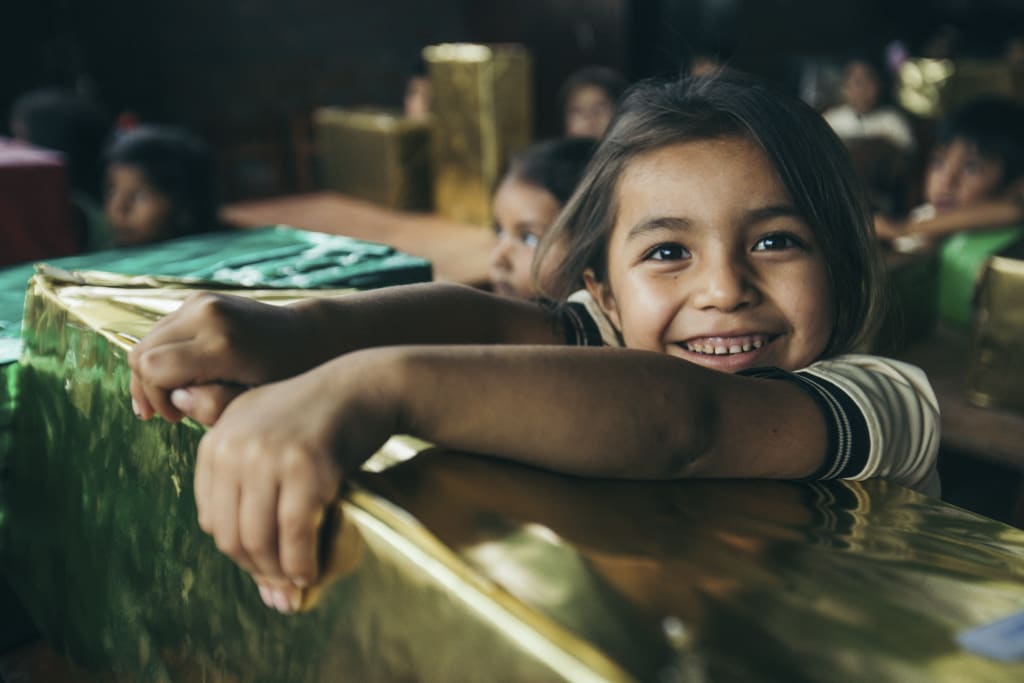 Little girl has a big smile on her face as she leans over her gold-wrapped present