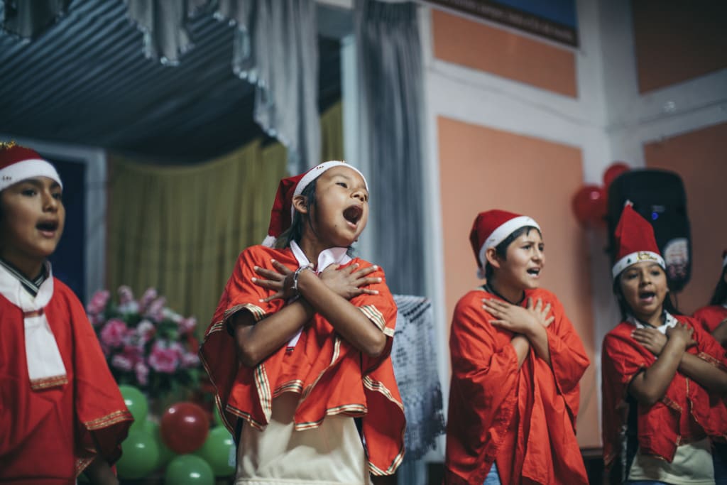 Children singing songs on the stage with santa hats, crossing their arms!