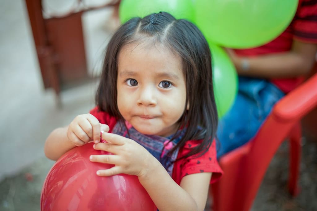Little girl wearing a red shirt is tying up a red balloon after blowing it up!