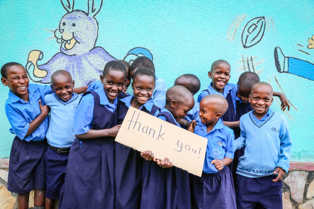 A group of Ugandan children in school uniforms hold a cardboard sign that says 'thank you'.