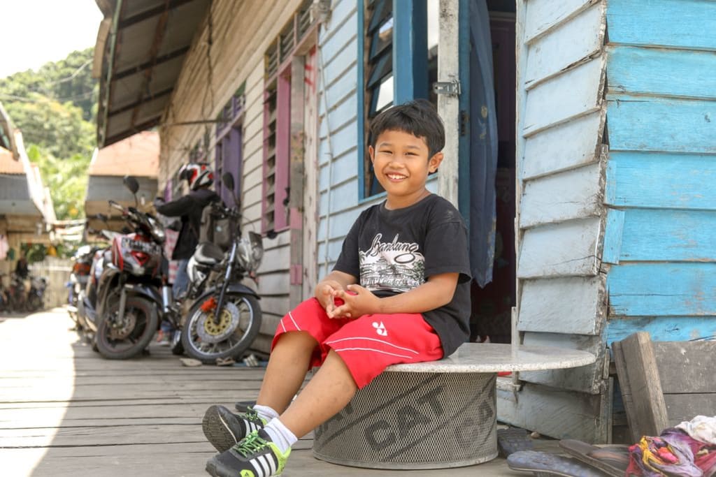 A little boy wearing red shorts and a black shirt smiles while sitting in front of motorbikes.