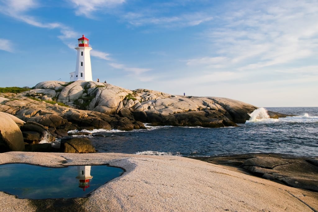 A picture of a white and red lighthouse on top of rocks by the ocean.