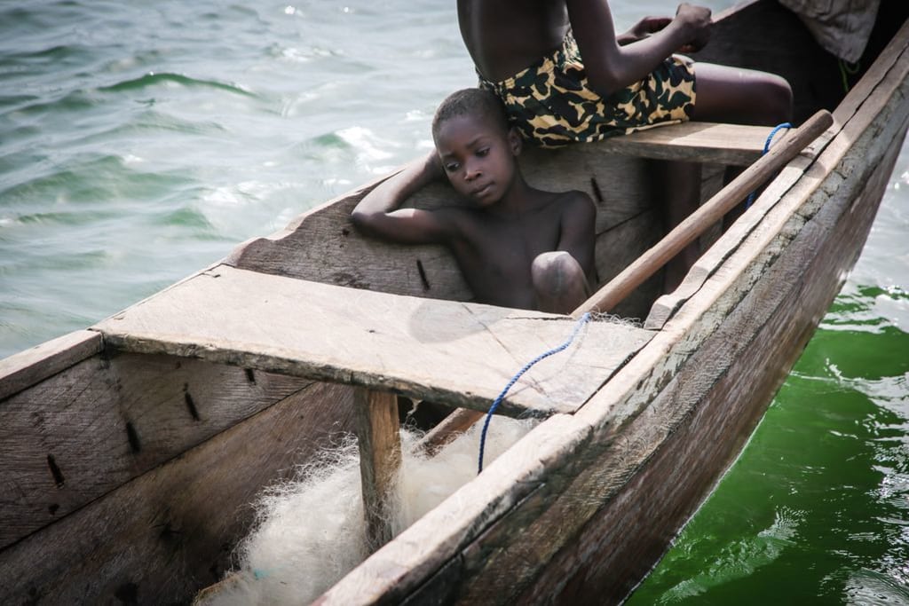 Little boy sits on the floor of the wooden fishing boat, looking sad.