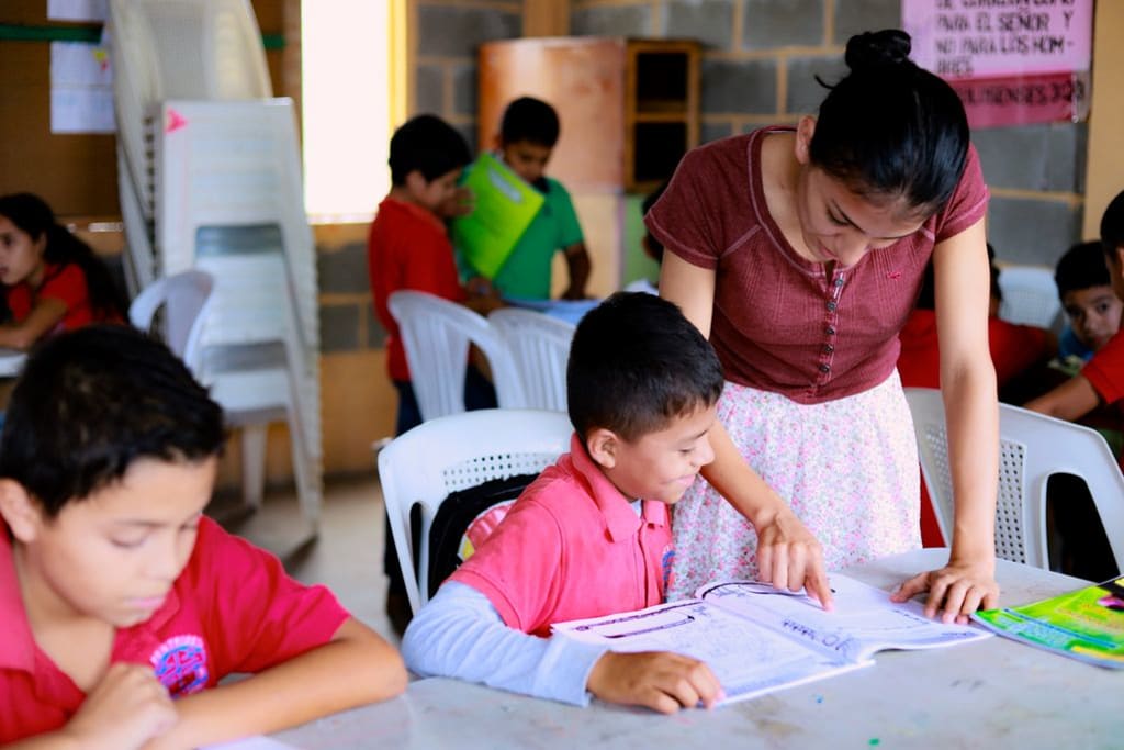 Débora, a tutor at a child development centre in Honduras, assists a child in writing a letter to his sponsor.