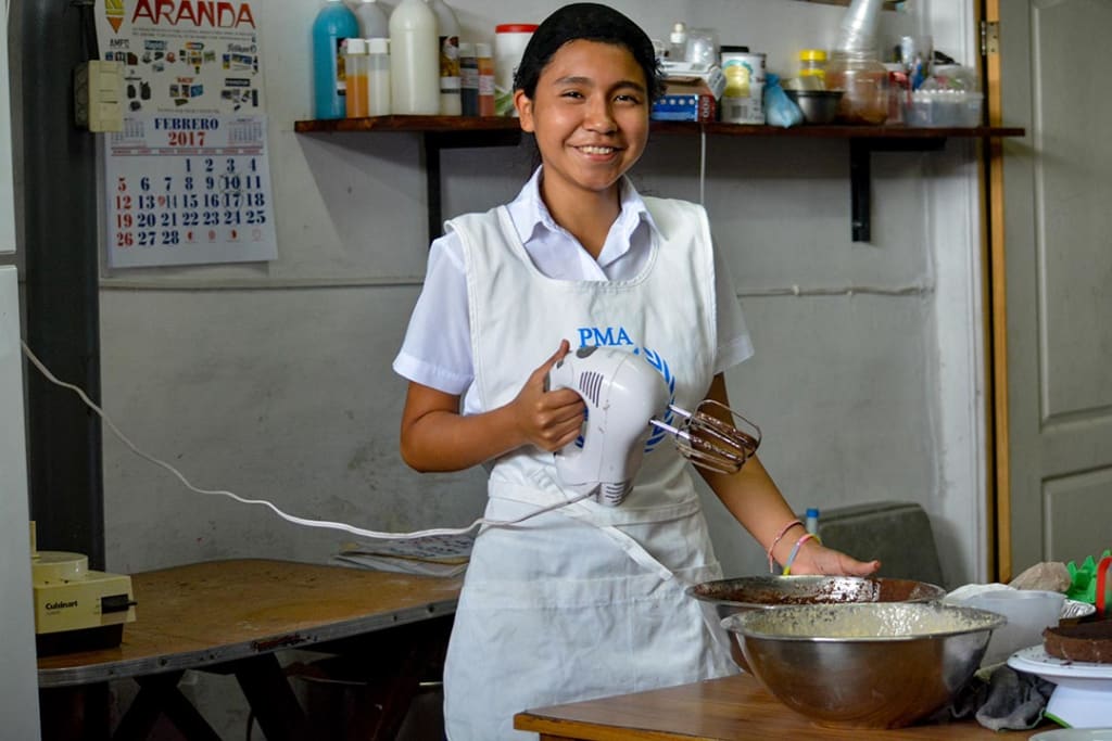 A teen girl holding a mixer in a bakery.