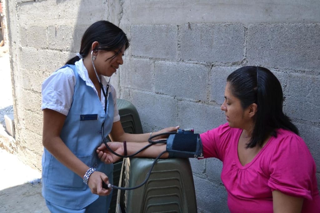 A young nurse in a nursing uniform, takes someone's blood pressure as they sit out on the street.