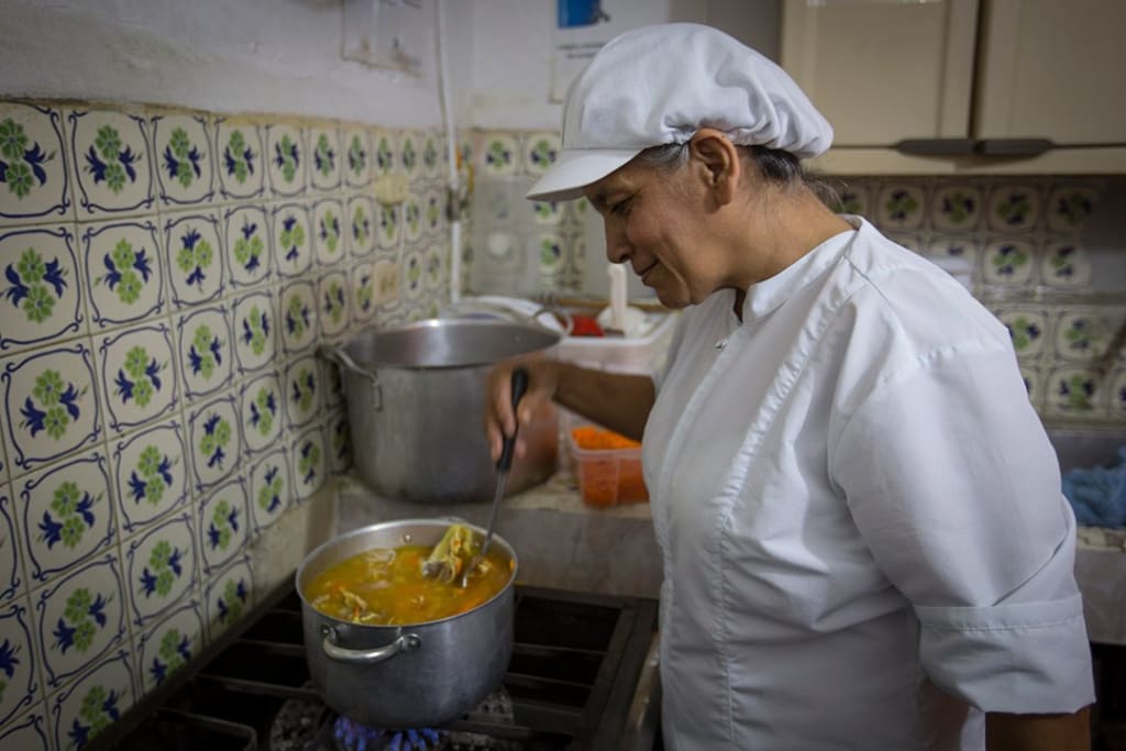 A compassion centre worker checks on the soup she's making for a special, Christmas meal. She stands in tiled kitchen and stirs the soup with her ladle.