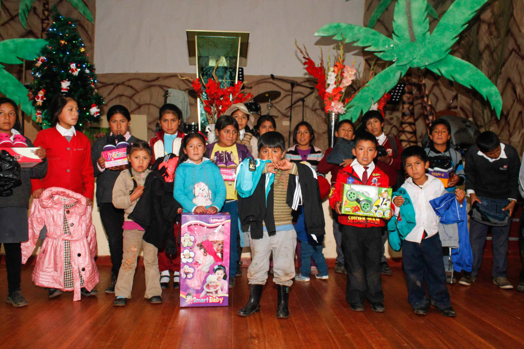 A group of kids pose with their Christmas gifts in their Compassion centre. There are pretend palm trees behind them.
