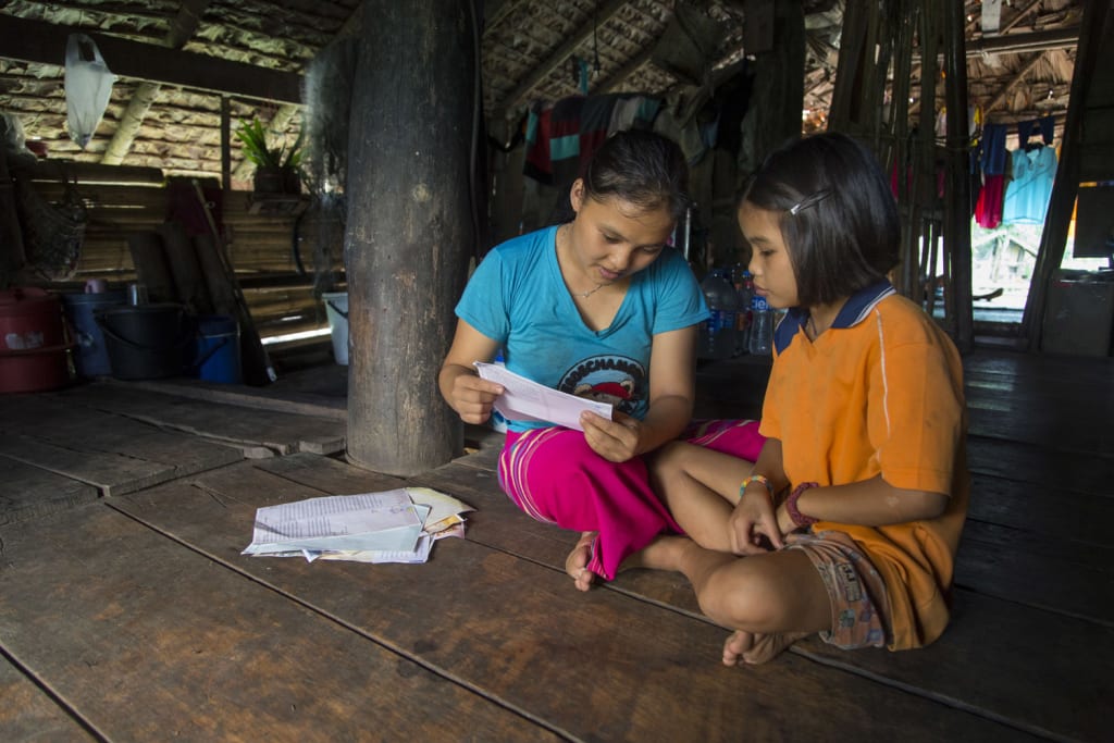 Two girls sit on the wood floor on their home while reading letters.
