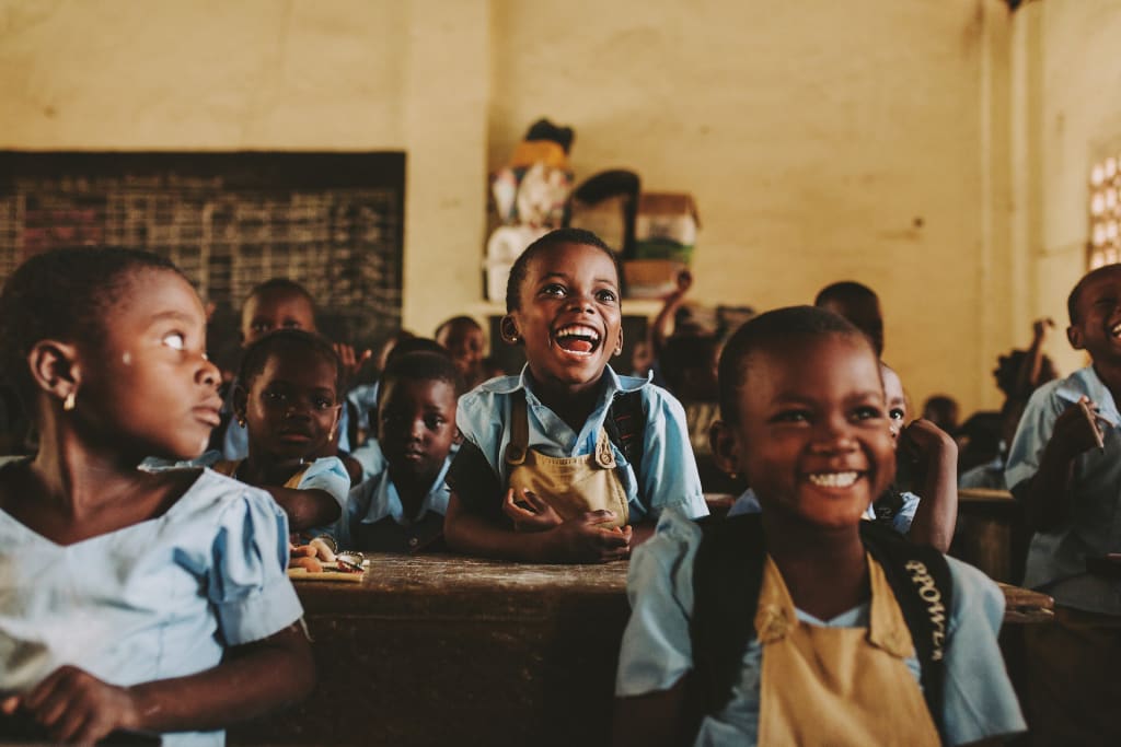 Elementary school students in a classroom in Togo smiling and laughing while sitting at their desks.