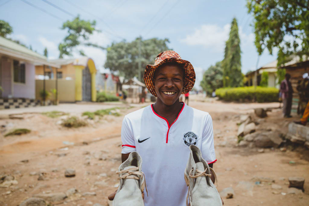 A young man from Tanzania holds up a pair of white shoes that he's made.