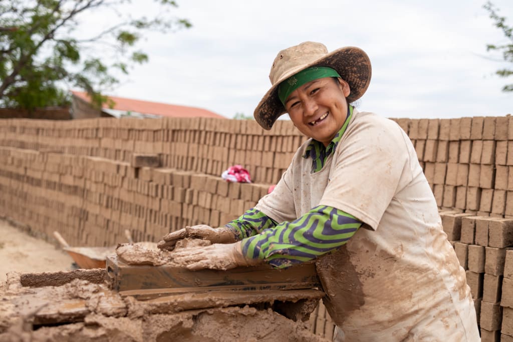 A woman is smiling while at work making bricks.