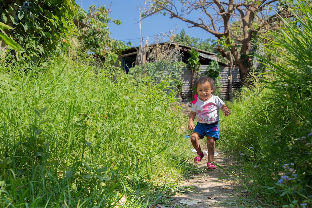 Little girl runs through grass smiling. She is wearing a t-shirt and shorts.